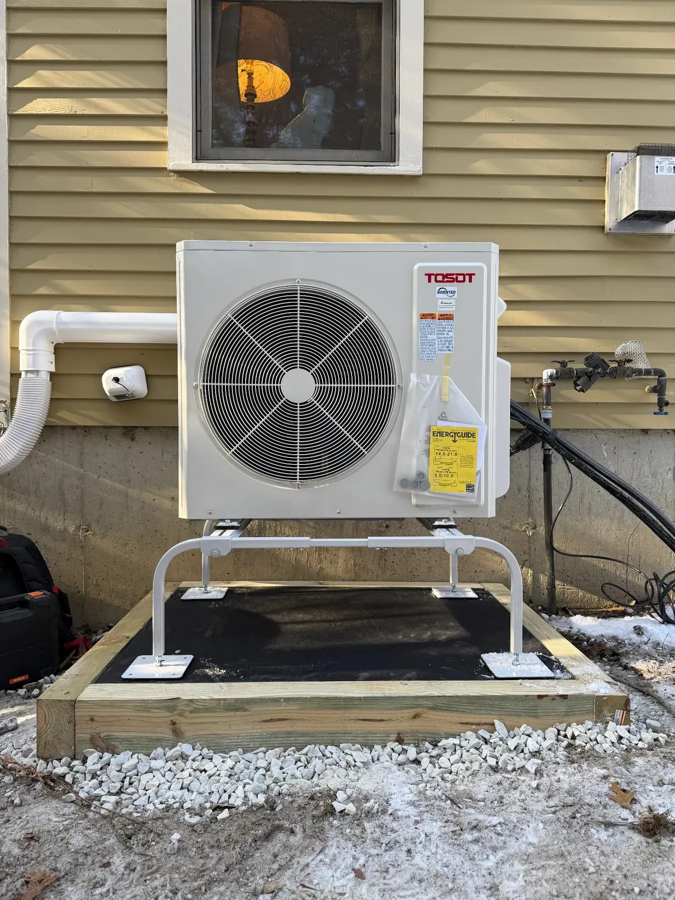 Tosot AC condenser installed on a raised pad beside a home