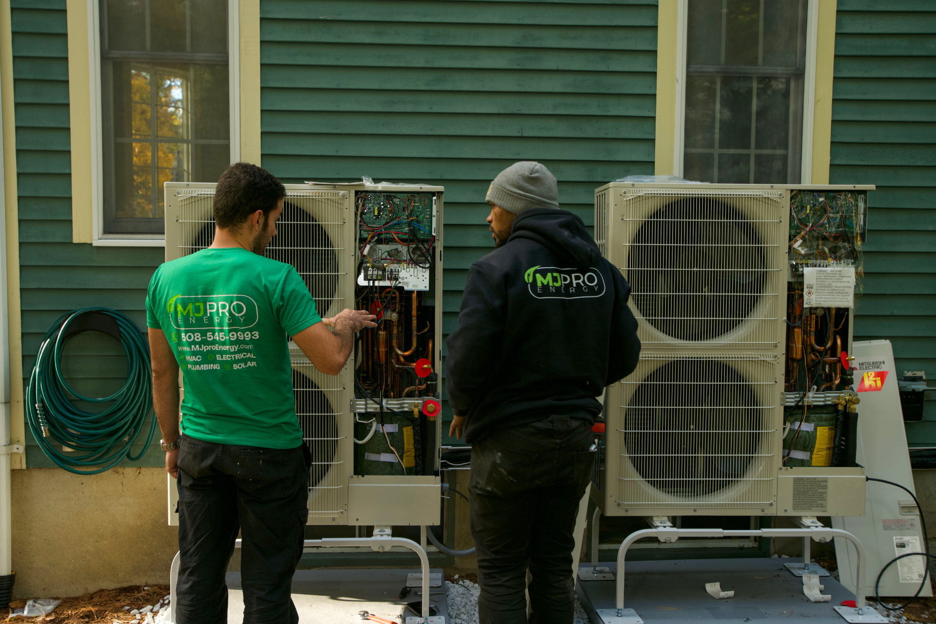 Two MJ Pro Energy technicians wiring Mitsubishi heat pump outdoor units